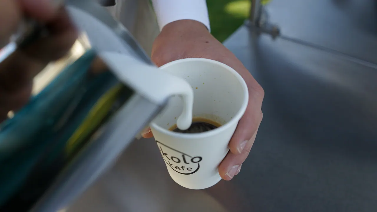 Detail nalévání napěněného mléka do kelímku s logem Okolo Kafe