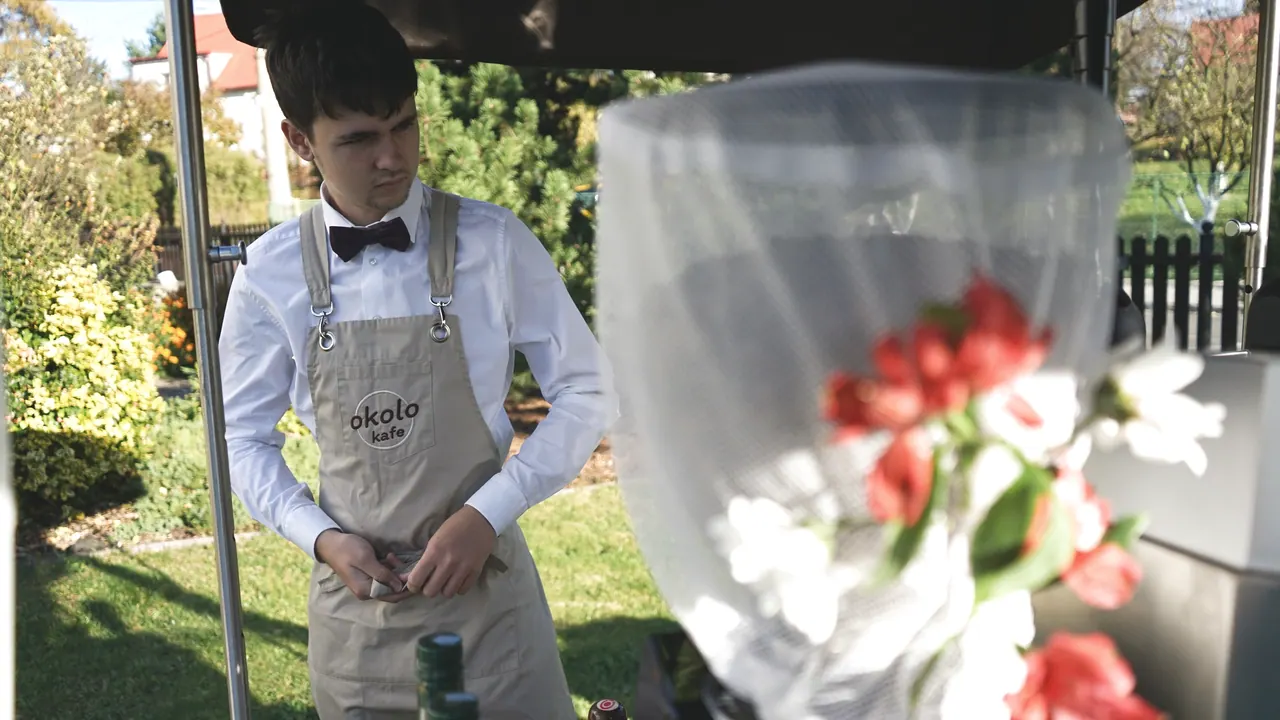 Barista v motýlku podává kávu vedle svatební kytice